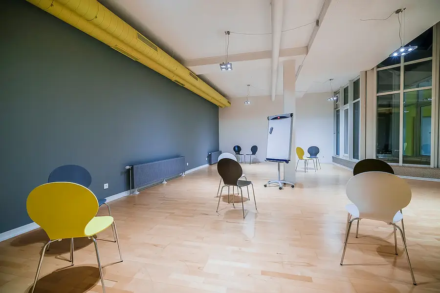 Proberaum mit verteilten Stühlen und Flipchart vor grauer Wand