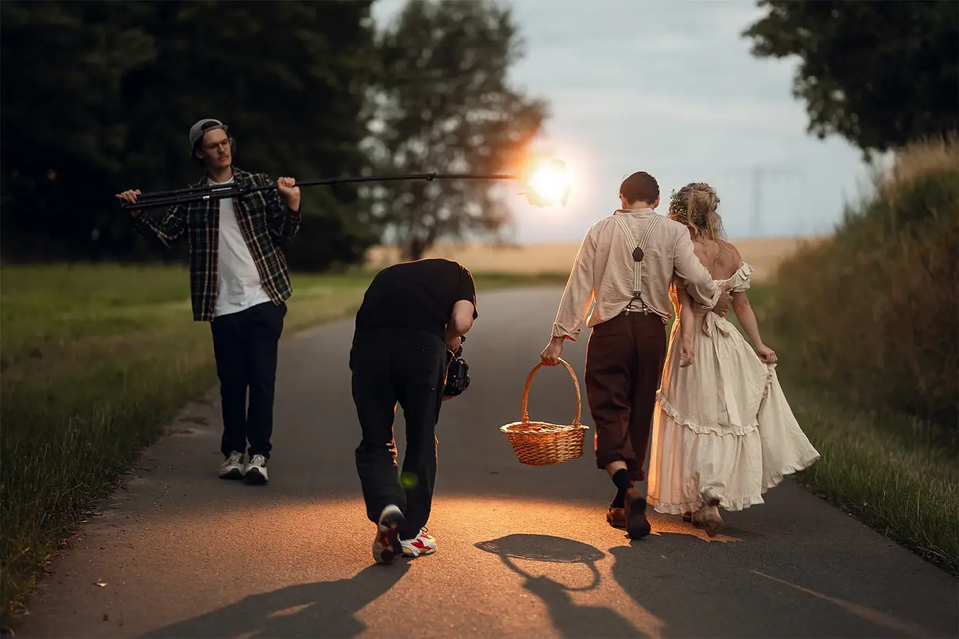 Filmteam dreht ein Paar in historischem Kostüm auf einem Feldweg bei Sonnenuntergang, Standbild aus dem IAF Abschlussfilm Musical 2025